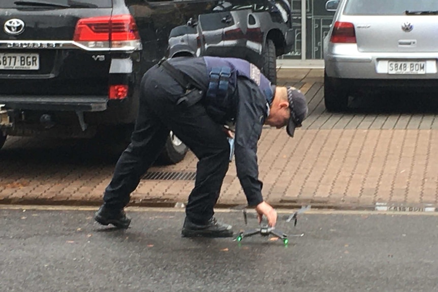 A male police officer places a small drone on a car park