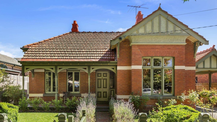 A historic double-fronted brick house sits behind a green picket fence and manicured front garden