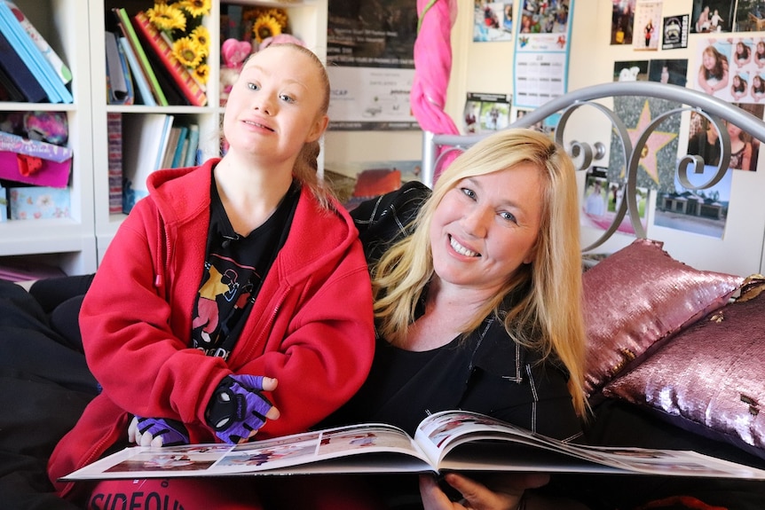 Ms Stuart sits on her bed at home with her mother, looking through her modelling portfolio.