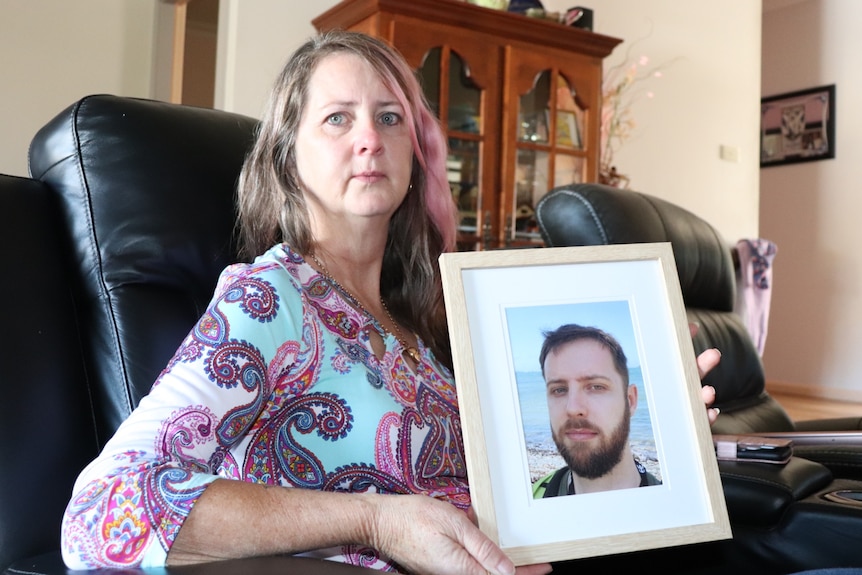 Woman holding framed photograph of young man.