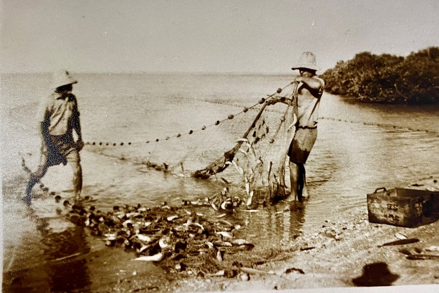 A black and white photo of two men dragging a net 