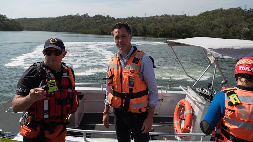 the new south wales premier chris minns with an ses personnel in a boat on the water ahead of an announcement
