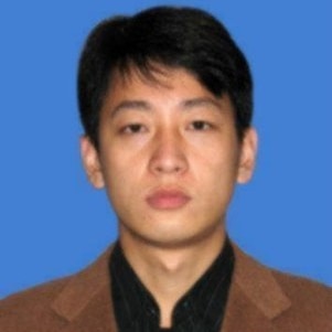 Headshot of an Asian man wearing a brown jacket and black shirt.