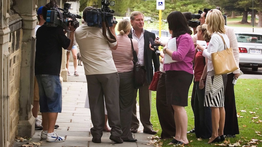 Journalists and camera operators surround Colin Barnett on a footpath.