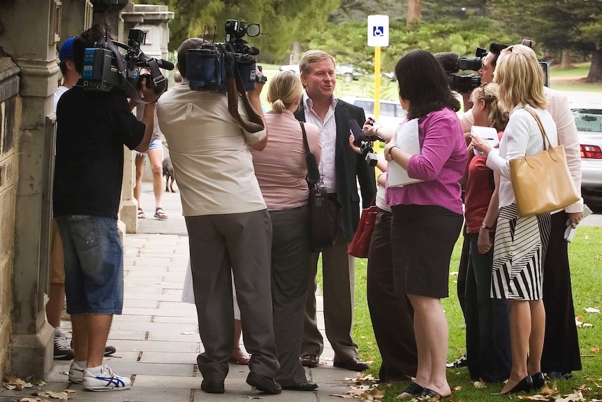 Journalists and camera operators surround Colin Barnett on a footpath.