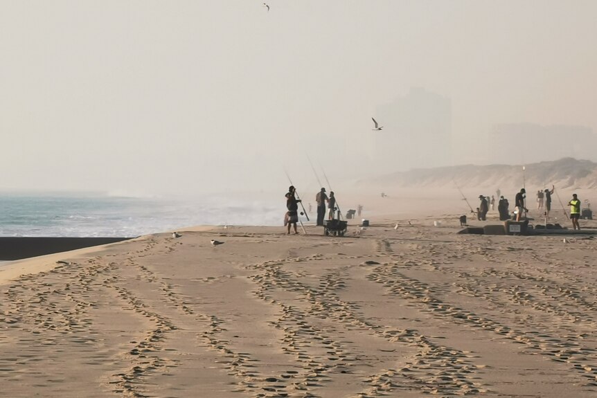 People standing on beach with fishing rods, amid smoke haze