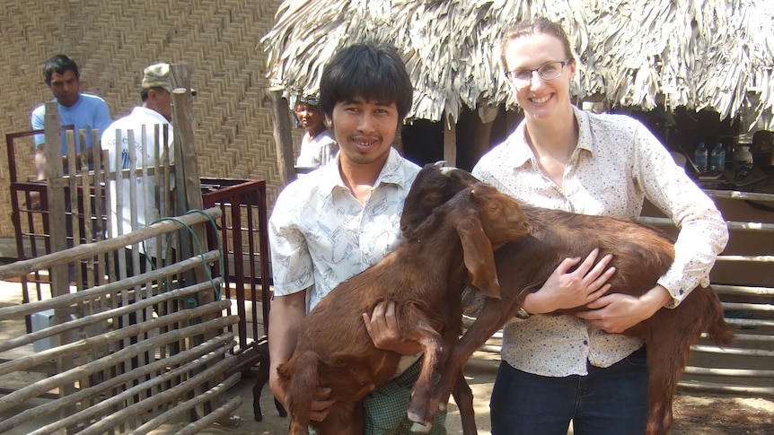 A woman stands next to a farmer each holding a goat 