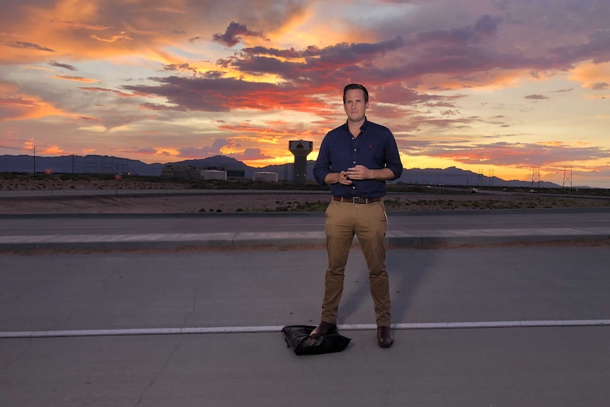 A man stands on a road in front of an orange sunset.