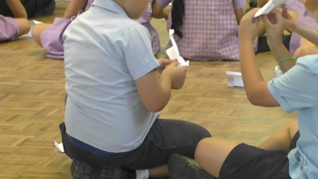 Children sit on floor and hold paper planes