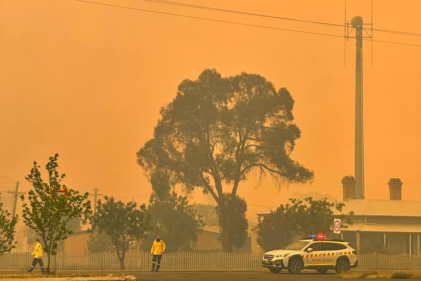 Emergency service personnel stand on a road in Wallangarra, the scene has an orange tint due to fires burning nearby