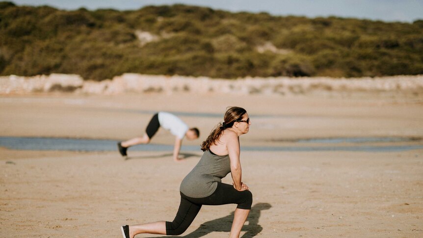 Woman lunging on beach with man in the background