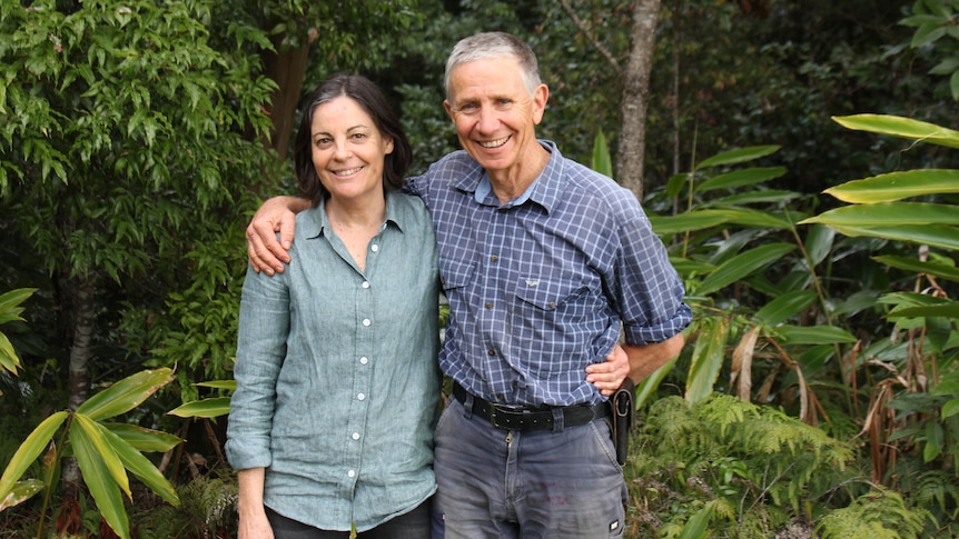 Smiling man and woman standing arm in arm with rainforest background.