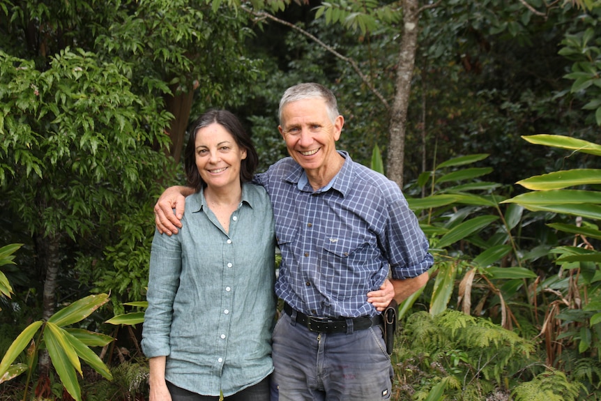 Smiling man and woman standing arm in arm with rainforest background.
