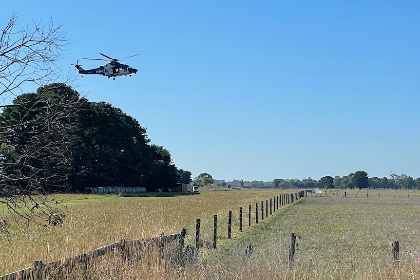 A helicopter flies overhead as emergency services inspect the scene of a light plane crash in the distance.