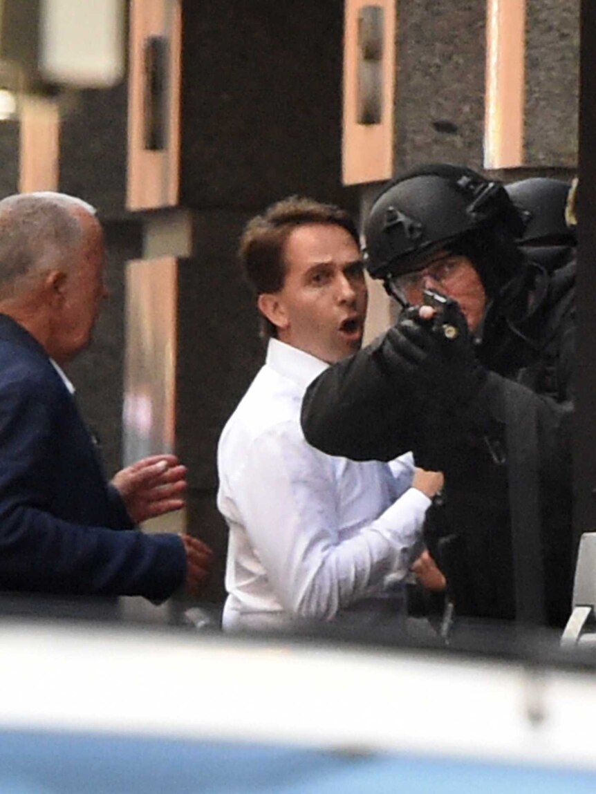 Stefan Balafoutis (R) and John O'Brien run for cover behind a policeman during a hostage siege in the Sydney CBD.