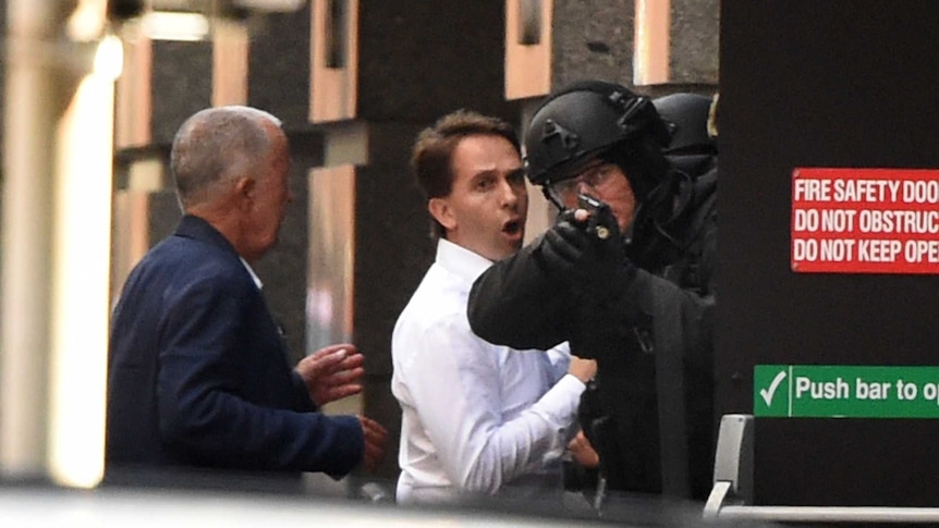 Stefan Balafoutis (R) and John O'Brien run for cover behind a policeman during a hostage siege in the Sydney CBD.