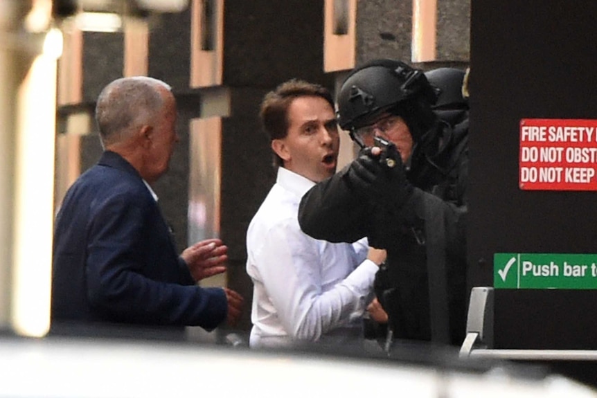 Stefan Balafoutis (R) and John O'Brien run for cover behind a policeman during a hostage siege in the Sydney CBD.