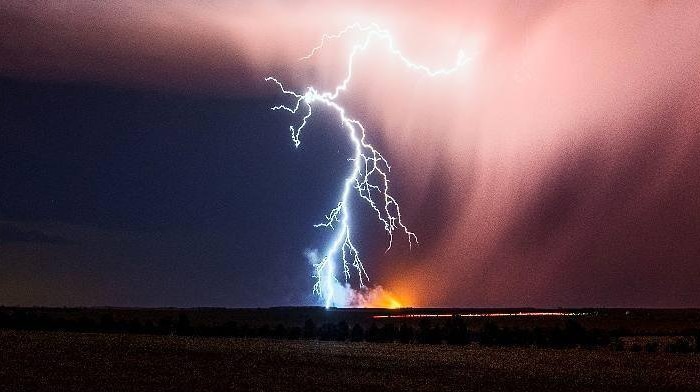 A fork of lightning strikes the ground in the distance, appearing to spark a fire on the horizon.
