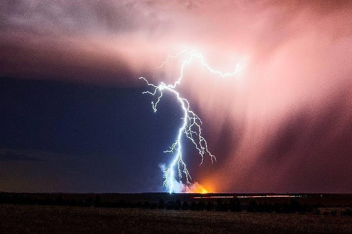 A fork of lightning strikes the ground in the distance, appearing to spark a fire on the horizon.