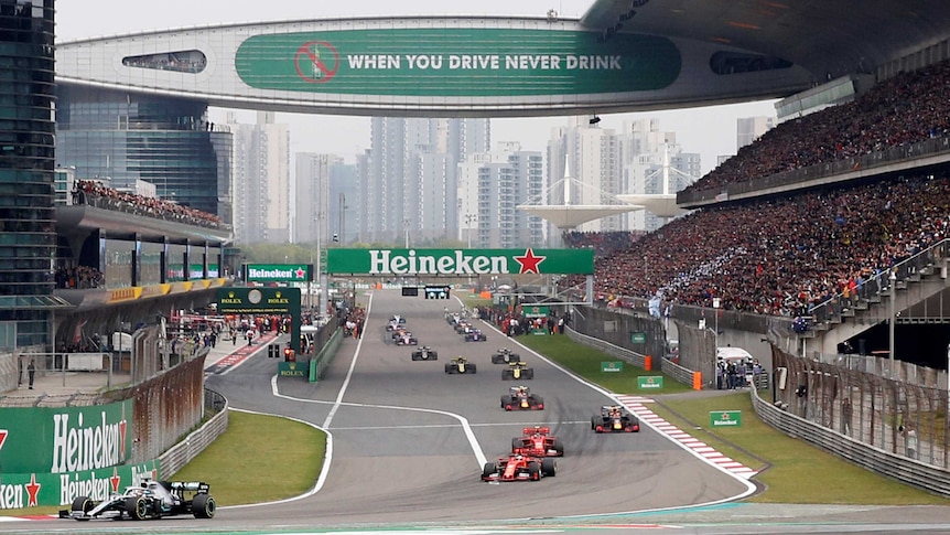 Formula One cars run down the straight before a Grand Prix in China, as fans pack the grandstands.