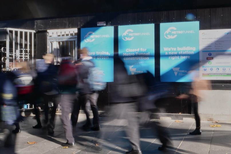 A blur of people walking down a footpath, with a construction site barrier in focus.