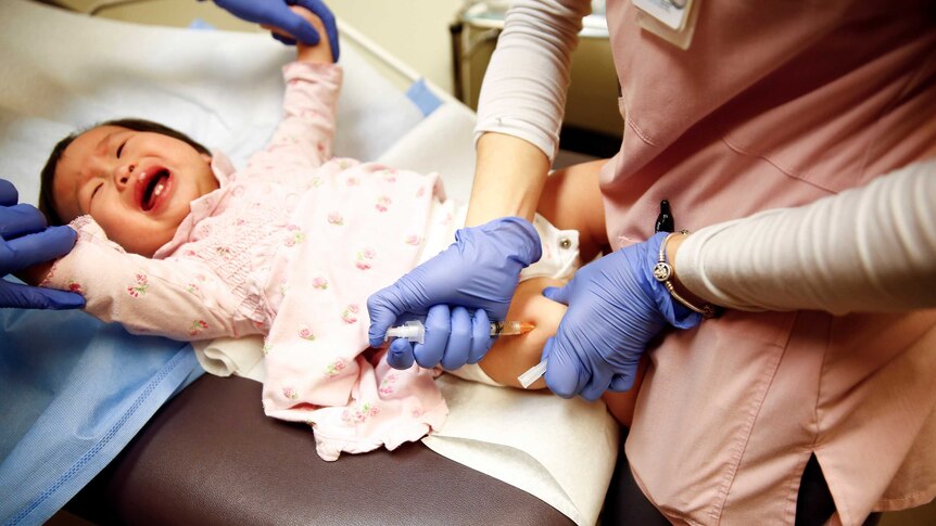 A baby cries while a doctor pushes a needle into her thigh