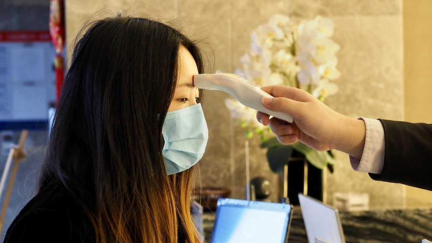 A hotel guest has a temperature measuring device placed on her forehead inside a hotel lobby