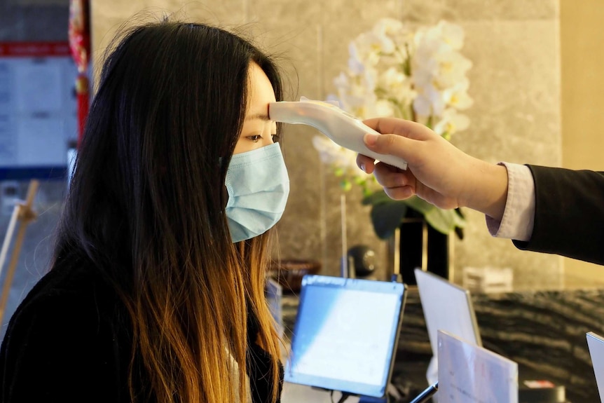 A hotel guest has a temperature measuring device placed on her forehead inside a hotel lobby