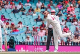 A spin-bowler completes his follow-through as the ball flies through the air in a Test match.