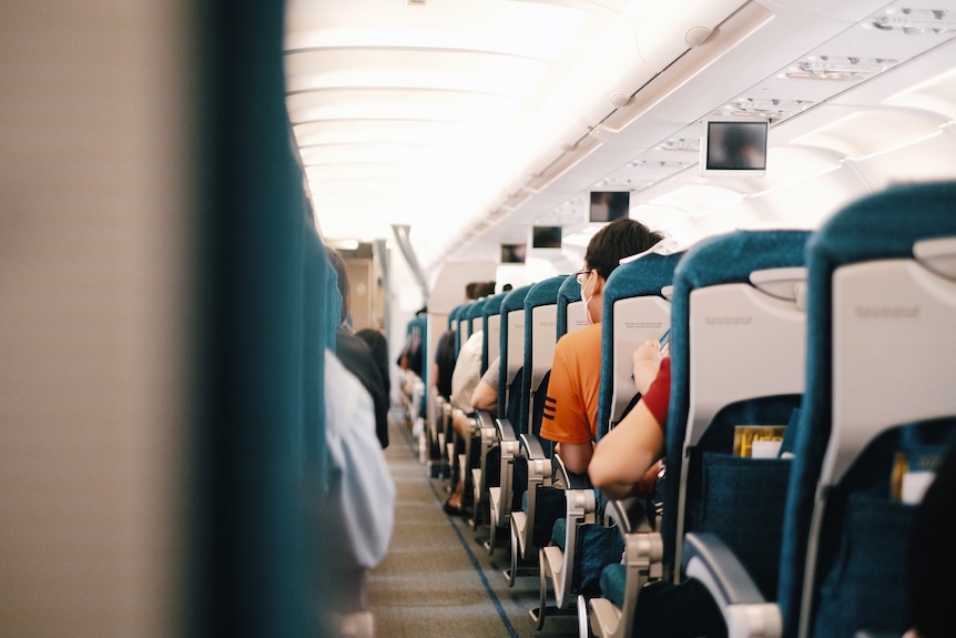 A photo of the middle aisle on a commercial flight, with people in casual clothing sitting in teal coloured seats