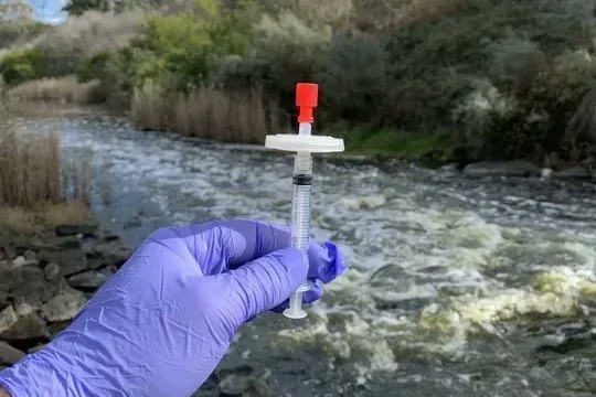 A gloved hand holding a small syringe