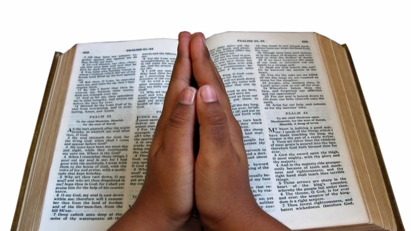 Hands praying over a Bible.