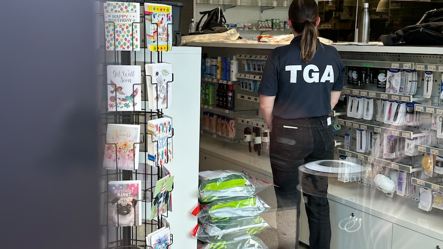 A woman in a TGA shirt is seen standing guard inside a pharmacy