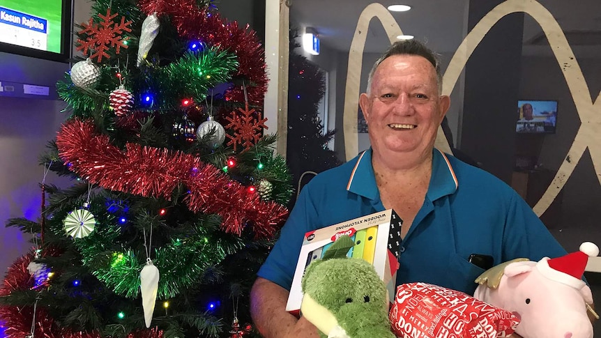A photo of Ken Muggeridge standing with an armful of presents in the ABC foyer.