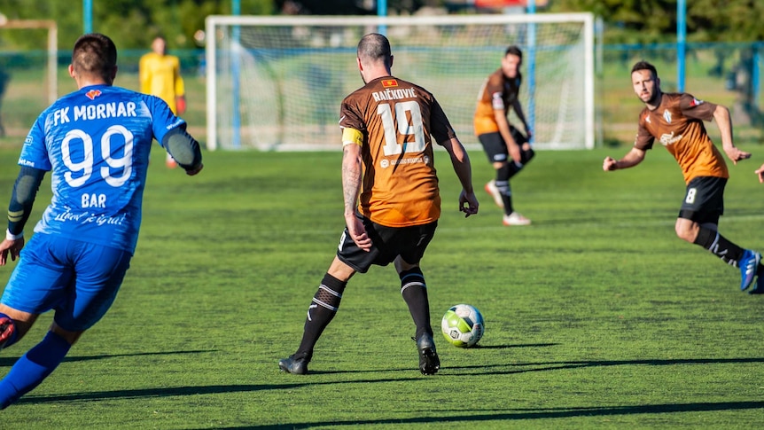 Three male soccer players in orange take on one in blue.