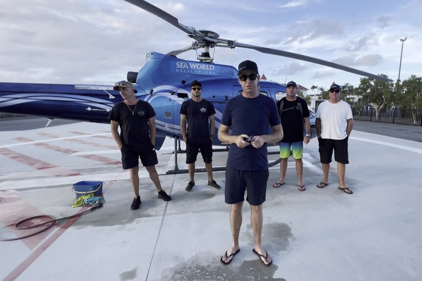Five men stand beside a helicopter
