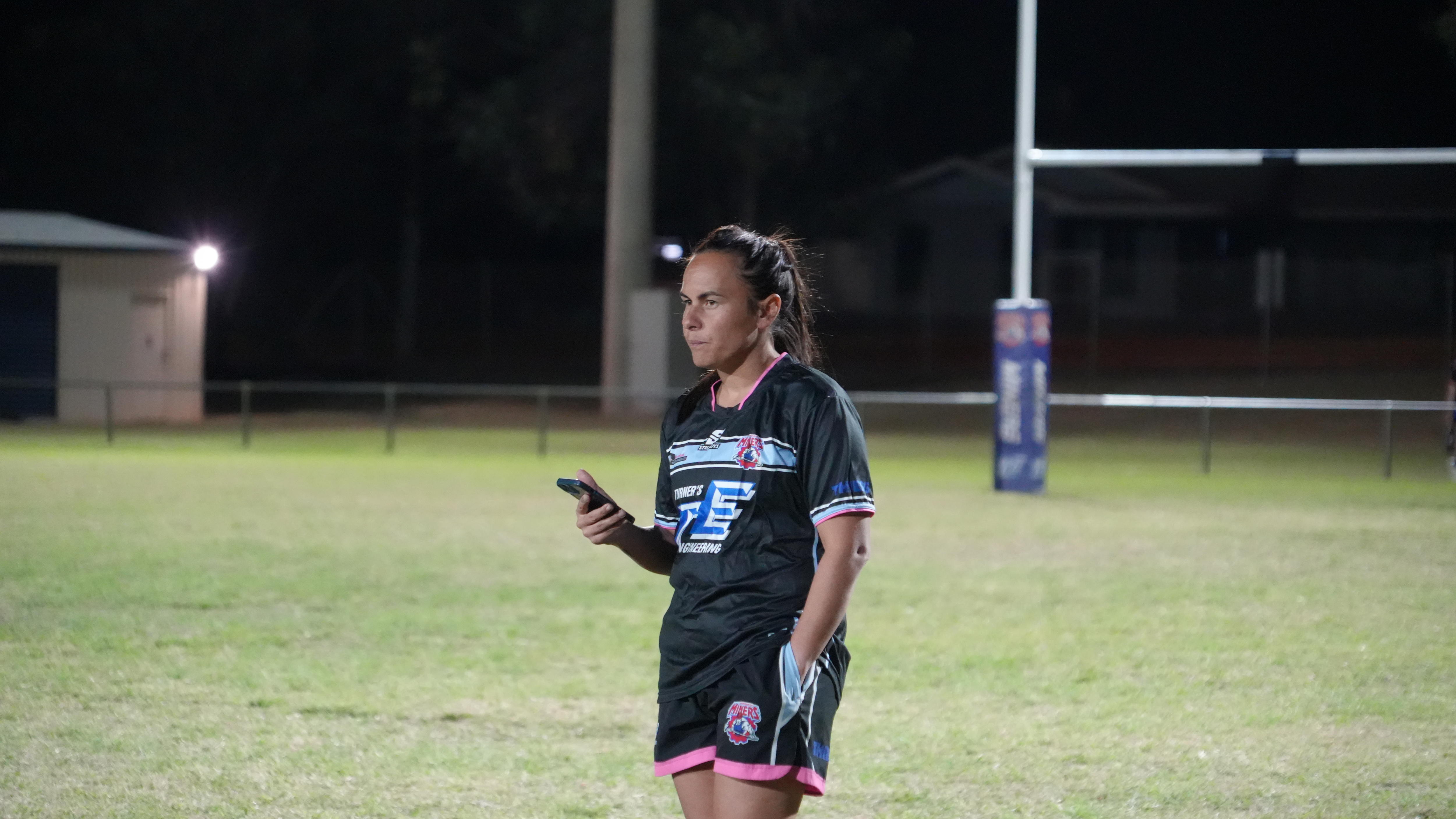 Coach holding phone in hand watching on football field, night time