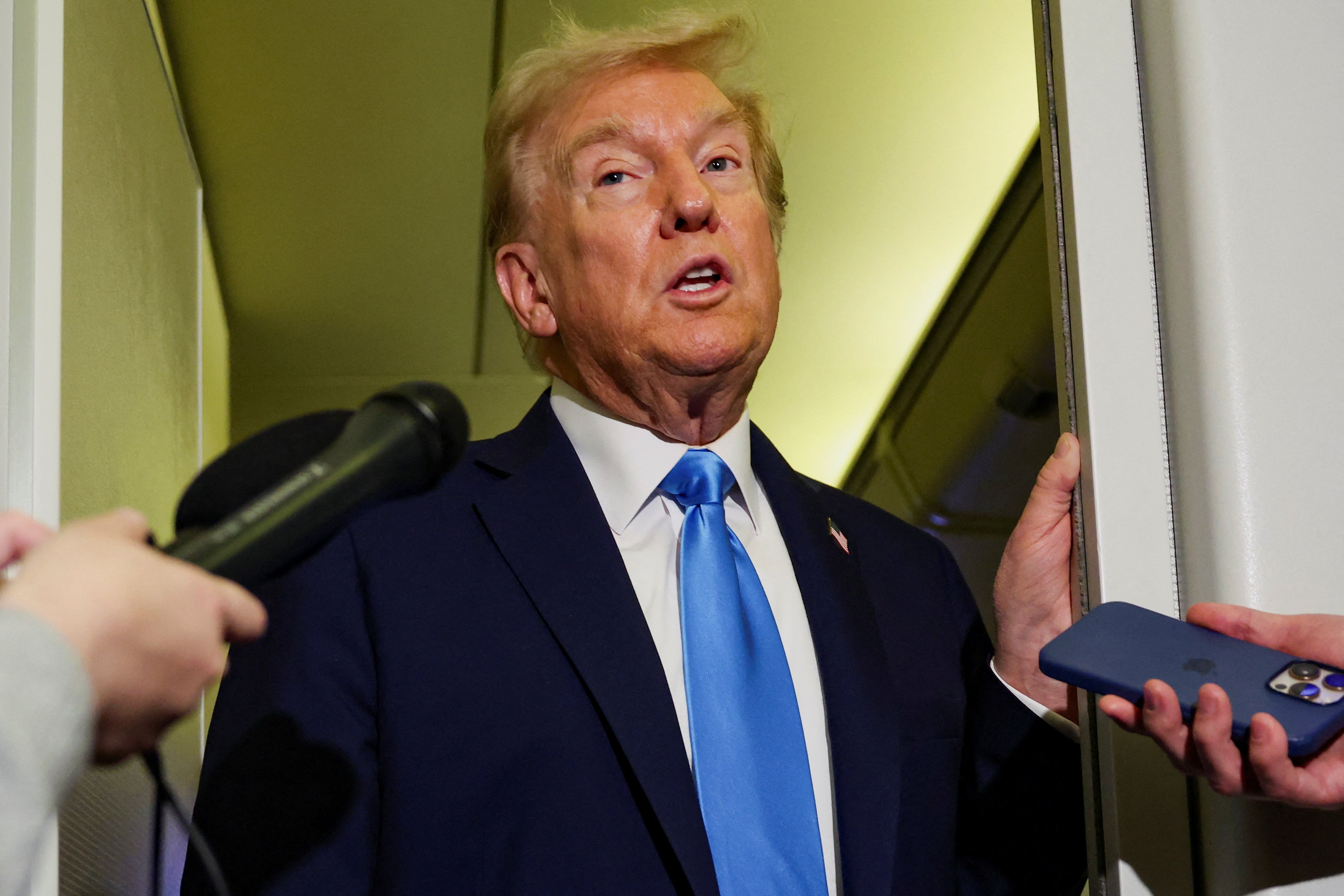 身穿西装、打着蓝色领带的唐纳德·特朗普扬起眉毛，对着麦克风讲话。