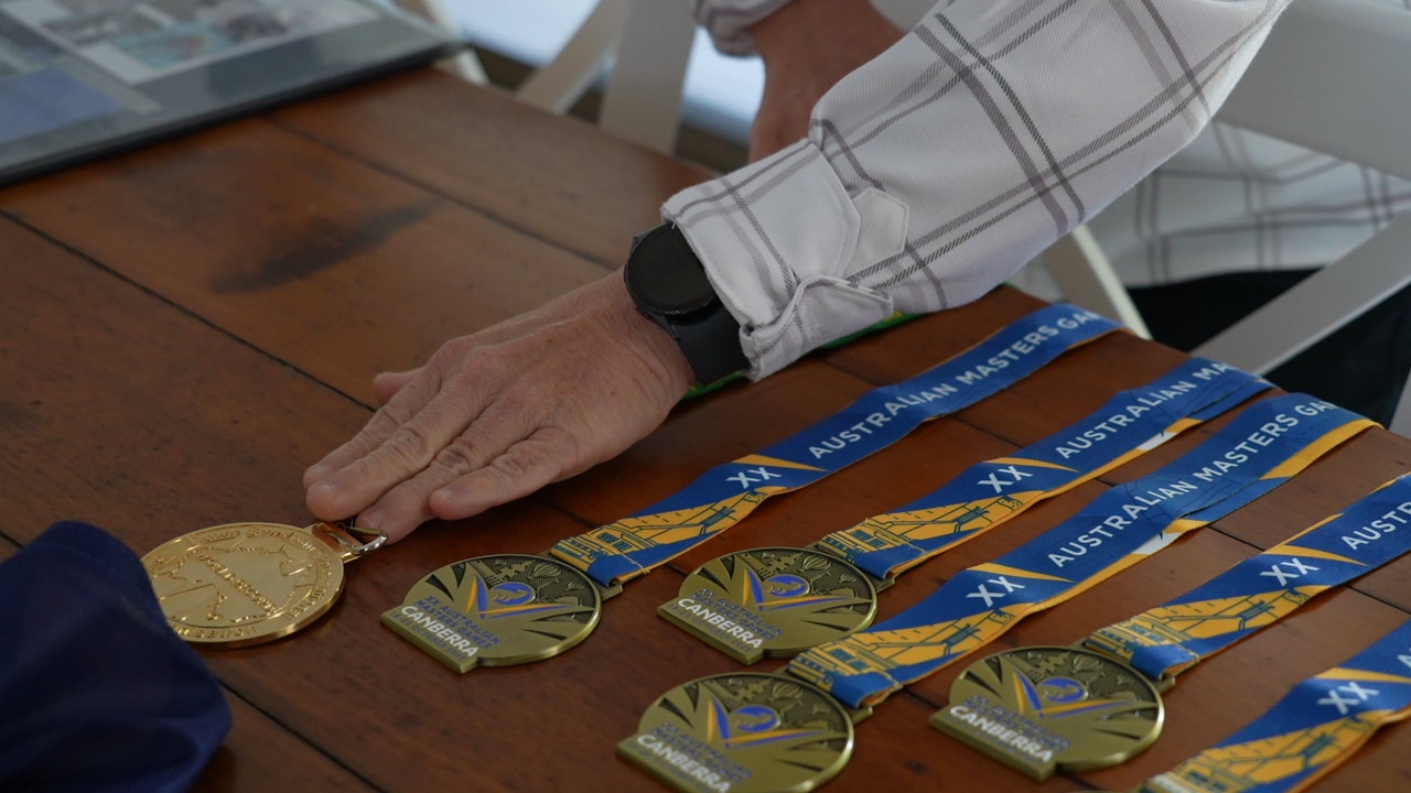 A close-up of a number of sports medals on a wooden table, a hand carefully laying them out.