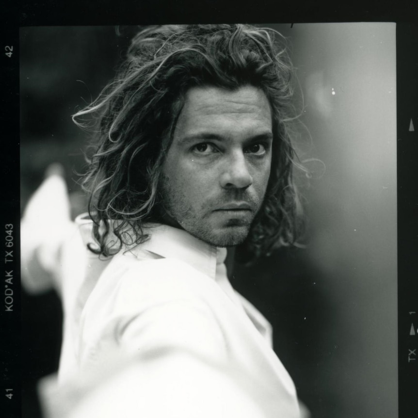 A black and white photo of Michael Hutchence wearing a white shirt fencing.