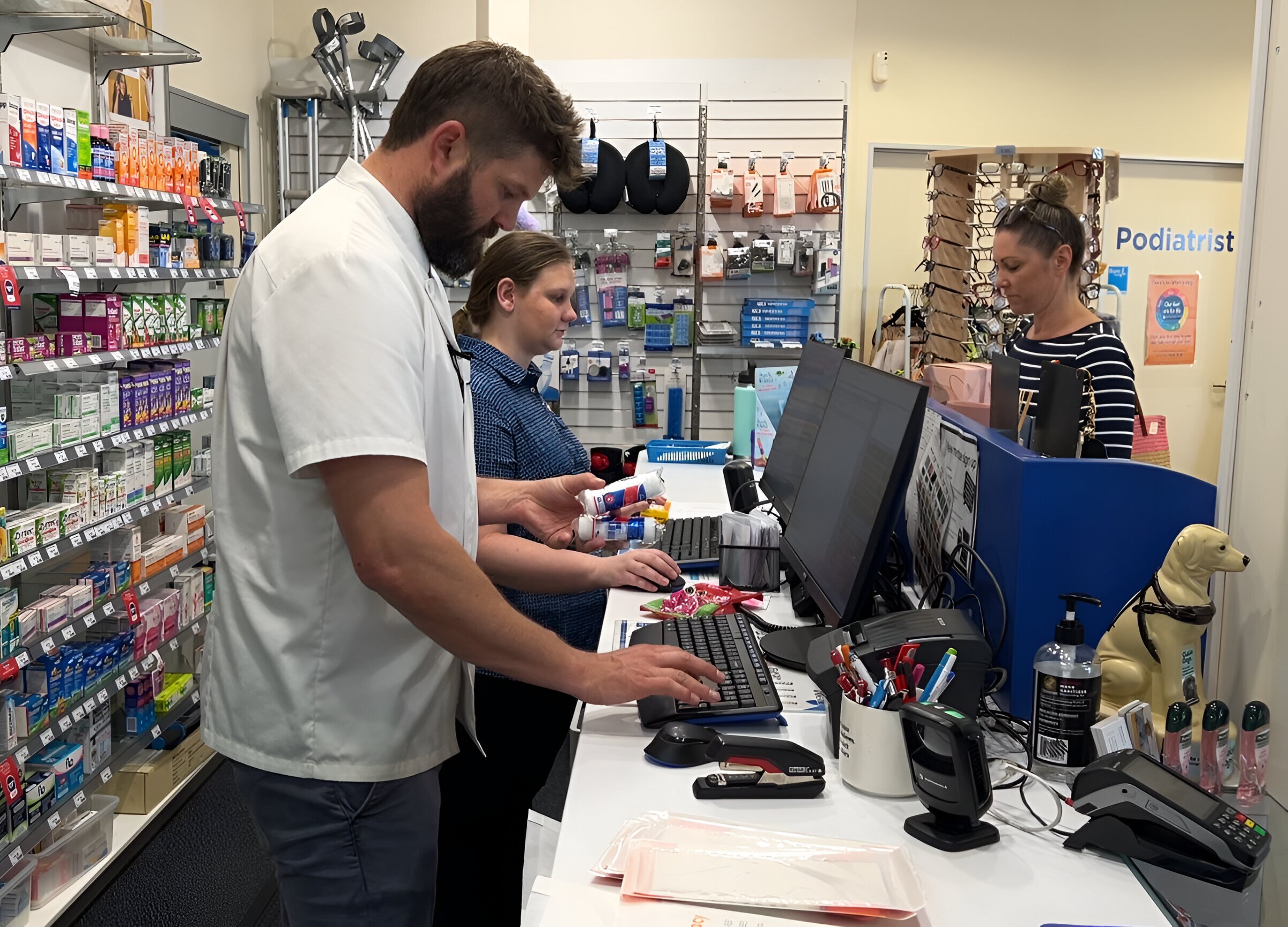 A pharmacist types while an assistant talks to a customer