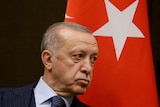 Turkish President Erdogan scowls near a Turkish flag.