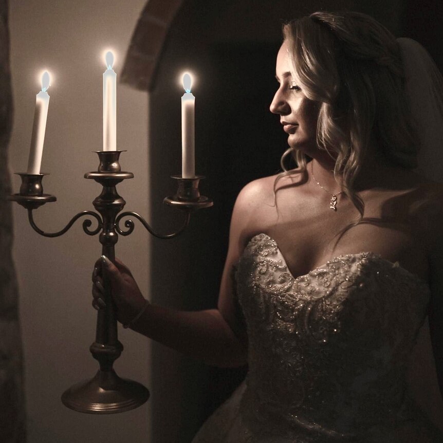 photo of blonde woman in a wedding dress holding a candelabra with three lit candles the light reflecting on her face