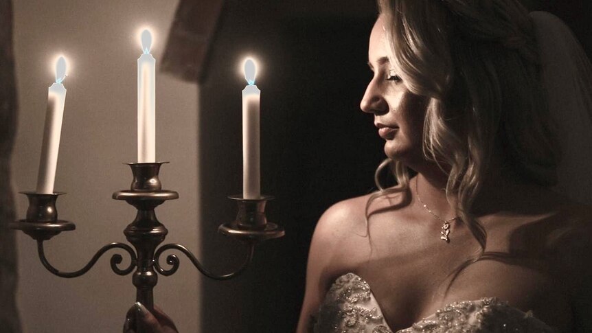 photo of blonde woman in a wedding dress holding a candelabra with three lit candles the light reflecting on her face