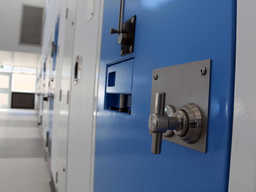 Doors to prison cells line a hallway.