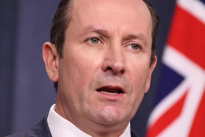 Mark McGowan at a press conference with a flag in the background.