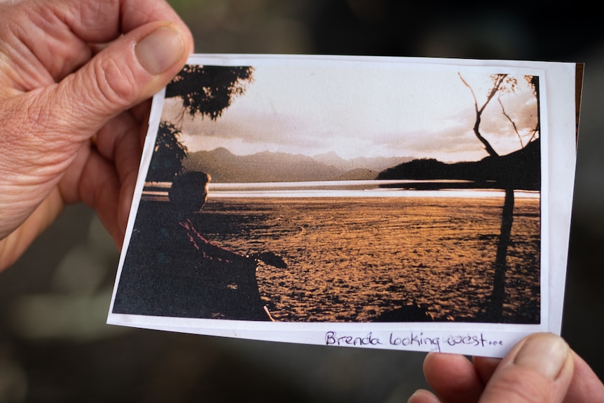 Woman holding an old photo of a woman on a beach. 