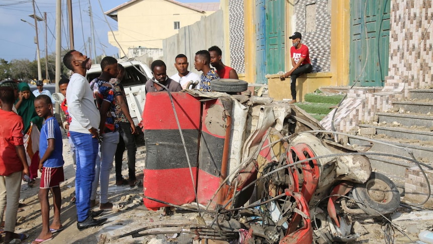 People stand around looking at a blown up car in front a restaurant in Somalia in March