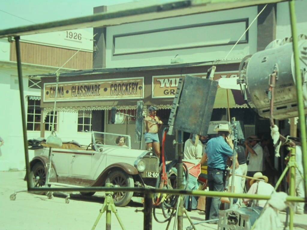 Green tinted photo of woman in vintage car with man in t-shirt and shorts holding a microphone above the car.
