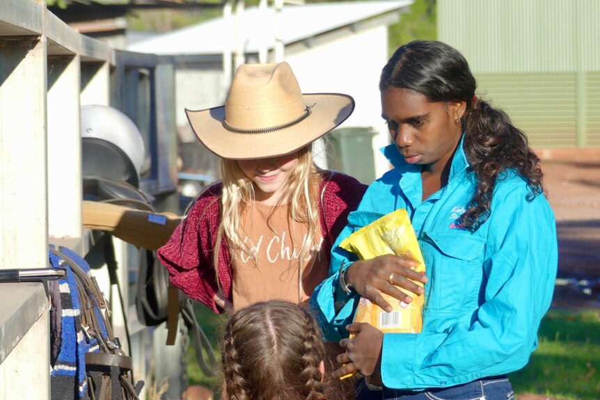 Three young girls facing each other with saddles nearby